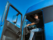 © Anna - A young man is a professional driver in the cab of a blue truck. Handsome Caucasian guy, a transportation worker sits in a big truck car