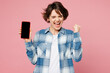 © ViDi Studio - Young woman wearing blue shirt white t-shirt casual clothes hold in hand use mobile cell phone with blank screen workspace area do winner gesture isolated on plain pink background. Lifestyle concept.