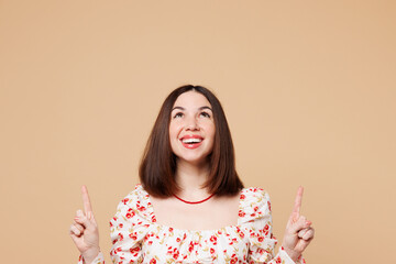 Poster - Young woman she wear white top casual clothes pointing index finger overhead indicate on workspace area copy space isolated on plain pastel light beige background studio portrait. Lifestyle concept.