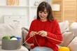 © New Africa - Beautiful woman knitting on sofa at home