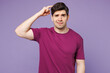 © ViDi Studio - Young sad mistaken Caucasian man he wearing violet t-shirt casual clothes holding put hand on head scratch temples isolated on plain pastel light purple background studio portrait. Lifestyle concept.