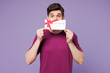 © ViDi Studio - Young man wear violet t-shirt casual clothes hold cover mouth with gift certificate coupon voucher card for store isolated on plain pastel light purple background studio portrait. Lifestyle concept.