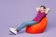 © ViDi Studio - Full body minded smiling happy young man he wear violet t-shirt casual clothes sit in bag chair hold hands behind neck head isolated on plain pastel light purple background studio. Lifestyle concept.