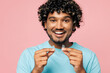 © ViDi Studio - Young smiling Indian man he wear blue t-shirt casual clothes hold in hand invisible transparent aligners, invisalign dental braces isolated on plain pastel pink background studio. Lifestyle concept.