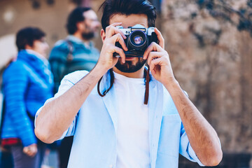 Wall Mural - Man lover of travel focusing to take photos walking on streets of downtown during summer holiday.Tourist photographer making pictures on vintage camera with modern lenses strolling in urban setting