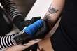 © New Africa - Professional artist tattooing woman's arm with machine in salon, closeup
