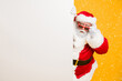 © deagreez - Portrait of funny funky santa claus in red headwear look behind white billboard wonder incredible 2020 christmas magic advents wear stylish black belt isolated over yellow color background