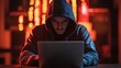 © Jittapon - Dramatic documentary style image of a cybercrime scene with a hooded hacker using a laptop in a dark and moody digital environment with dramatic lighting and shadowy ominous atmosphere