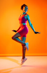 Sportive black hispanic woman wearing sportswear training in fitness studio, colorful dramatic lighting - African-american female athlete doing sport workout