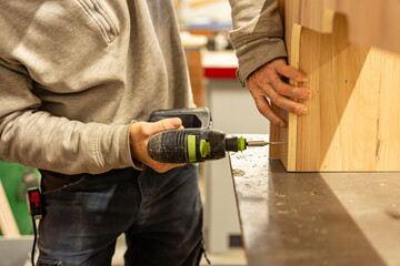 Ouvrier artisan blanc expérimenté en train d'utiliser des outils et une perceuse pour la fabrication d'un meuble en bois dans son atelier 