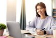 © Prostock-studio - Home Office And Telecommuting Concept. Potrait of smiling casual woman sitting at desk, using laptop. Female writing in notebook, taking notes, working or studying remotely, free space