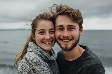 Wall Mural - Portrait of a grinning couple in their 20s showing off a thermal merino wool top on serene seaside background