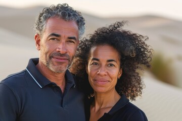 Wall Mural - Portrait of a blissful multicultural couple in their 40s donning a classy polo shirt isolated on serene dune landscape background