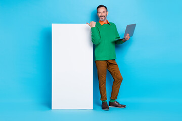 Full length photo of mature nice mister hold netbook point vertical billboard dressed stylish green look isolated on blue color background