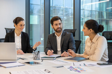 Wall Mural - Colleagues engaged in business meeting in modern office. Discussion on strategy, collaboration, interaction. Business man and women in formal attire. Laptop, tablet, phone on table.