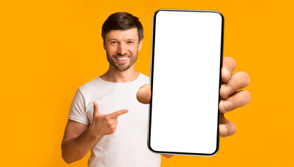 Wall Mural - Recommendation. Portrait of excited bearded man holding big smartphone with white blank screen in hand, showing close to camera and pointing at device. Gadget with empty free space for mock up, banner