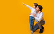 © Prostock-studio - Excited cute little girl pointing her daddy at copy space over yellow background, showing nice offer, discounts for kids