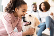 © Prostock-studio - Portrait of smiling African American girl whispering something in the ear to her pet, telling secret and emracing happy dog, spending time together with best friend in living room, selective focus