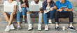 © Prostock-studio - Teen pastime. Group of teenagers spending time outdoors, sitting with gadgets on stairs, panorama