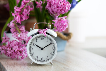 Wall Mural - Spring change, Daylight Saving Time concept. White alarm clock and hyacinth flowers on the wooden table. Springtime home gardening, hobby, leisure. Copy space for text