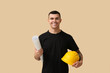 © Pixel-Shot - Young male engineer with hardhat and blueprint on beige background