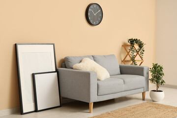 Beautiful living room with grey sofa, pictures and clock on beige wall