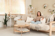 © Pixel-Shot - Young woman sitting on beige couch in living room