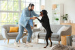 © Pixel-Shot - Young man in headphones with Dobermann dog dancing at home