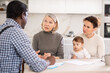 © JackF - Attentive old and middle-aged women sitting with an infant in the kitchen with sheets of paper in front of them talking to male agent