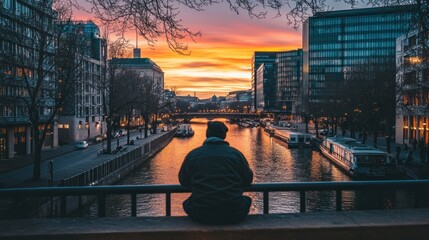 Fototapete - A person gazes at a vibrant sunset over a city river, reflecting on the day's end.