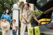 © DragonImages - Family getting ready for vacation by packing suitcases into SUV. Parents and child engaging in loading luggage while standing outside house