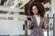© Tetiana - Serious young African American business woman walks into office building, opens glass door, holds and uses mobile phone