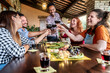 © charmedlightph - Young people having dinner party sitting in bar restaurant porch - Happy friends having fun toasting and drinking red wine at winery vineyard - Concept about enjoying harvest together at farmhouse