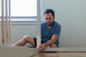 Wall Mural - A man is sitting on the floor and fixing a piece of furniture