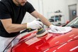 © SerPak - A technician attentively polishes the hood of a bright red car using a rotary buffer at an auto detailing shop. The workspace is well-lit and clean, showcasing the focus on vehicle maintenance and car