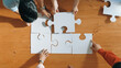 © Summit Art Creations - Top down view of skilled business people assemble jigsaw puzzle on meeting table. Group of diverse team working together to solve the puzzle. Represented unity, togetherness, cooperative. Convocation.
