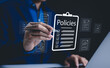 © Supatman - Policy documentation and compliance concept. A person reviews digital document labeled 'Policies' with icons, checklists, certifications, and financial detail. policy management, regulatory compliance