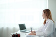 © Treerat - A woman is sitting at a desk with a laptop and a pen