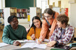 © Mediaphotos - Group of diverse students collaborating on academic project in modern library setting. Friendly, engaged discussion happens around table with open books and notebooks