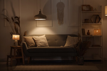 Wall Mural - Interior of living room with cozy sofa, pampas grass, shelving unit and glowing lamps