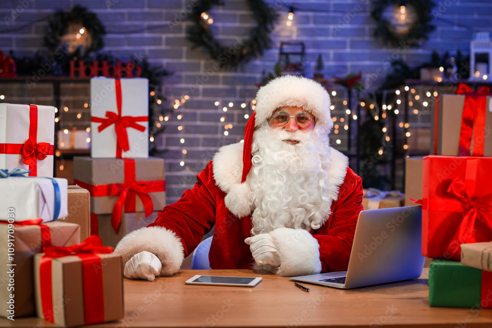 Santa Claus with laptop, tablet computer and gift boxes in post office