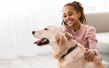 Wall Mural - Bonding, Togetherness And Friendship. Smiling African American girl stroking and playing with her happy dog in collar in living room at home, sitting on gray rug floor carpet