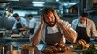 ©  Shomixer - In a busy kitchen environment, a cook looks distressed with hands on his head, surrounded by cooked dishes, while two chefs prepare meals in the background.