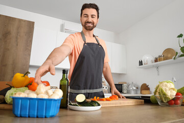 Wall Mural - Handsome bearded man with fresh vegetables cooking in kitchen