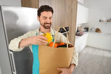 Wall Mural - Handsome bearded man with bag of food near fridge in kitchen