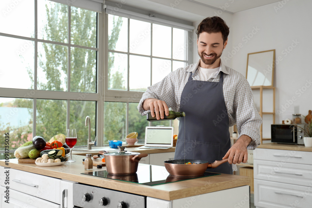 Handsome bearded man pouring olive oil on frying vegetables in kitchen