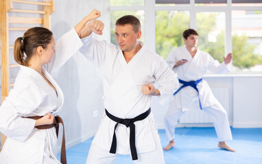 Wall Mural - Woman and man in kimono sparring together in gym during karate training