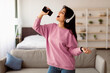 © Prostock-studio - Carefree Singer. Portrait of young lady singing favorite song and using cell phone as a microphone, dancing and wearing wireless headset. Excited woman having fun at home, enjoying sound