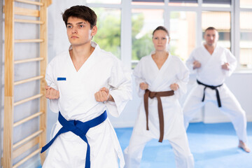 Wall Mural - Woman and man in kimono standing in fight stance during group karate training