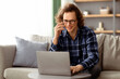 © Prostock-studio - Freelancer Guy Talking On Cellphone Using Laptop Sitting On Sofa Indoor, Working Online Remotely From Home. Hipster Man Having Phone Conversation Communicating And Browsing Internet On Computer